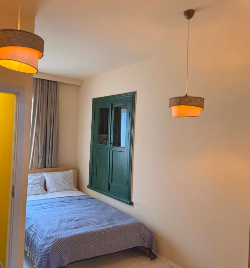 Compact bedroom with cream walls, two woven pendant lamps, and original green-painted shutters set into the wall